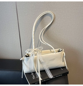 Detail of minimalist cream shoulder bag with long straps and lace bow decoration