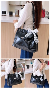 Détail du sac cabas noir brillant avec nœud en dentelle et bandoulière en chaîne