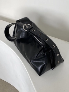 Detail of glossy patent leather shoulder bag with wide strap and silver metal eyelets