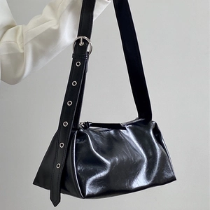 Detail of black glossy pleated shoulder bag with wide strap and silver metal eyelets