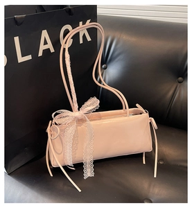 Detail of pink faux leather shoulder bag featuring a white lace bow and side drawstring