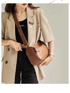 Close-up of caramel brown leather shoulder bag with wide strap and gold triangle buckle
