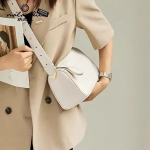 Detail of minimalist cream leather cylindrical crossbody bag with gold hardware on model