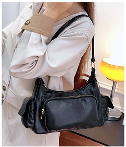 Detail of a vintage black faux leather shoulder bag with gold zippers worn by a model