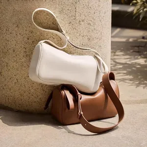 Minimalist soft leather pillow bags in cream and tan leaning against a stone pillar