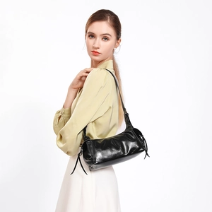 Glossy black pleated shoulder bag with long tassel detail on a fashion model