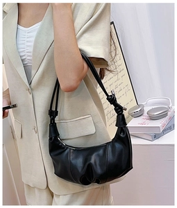Detail of black crescent croissant bag with knot handle worn by a model in a beige suit