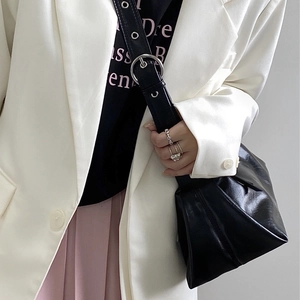 Detail of a black leather underarm bag with a wide strap and large round metal buckle