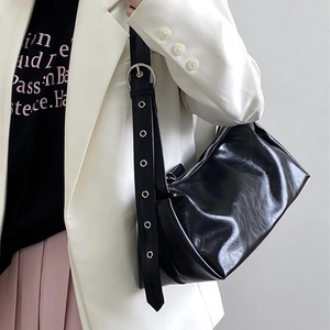 Detail of black pleated faux leather bag with silver eyelets on wide strap