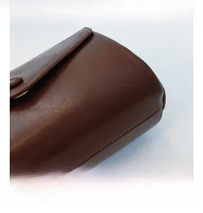Close-up of brown leather bag showing fine stitching and round magnetic buckle detail