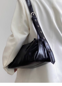 Close-up of black glossy shoulder bag with wide strap featuring silver metal eyelets