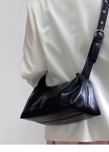 Detail of glossy black underarm bag featuring wide strap with metal eyelets and sleek finish