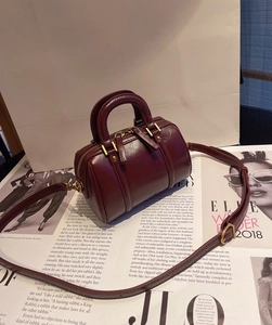 Close-up of a burgundy leather Boston bag with gold hardware on a fashion magazine