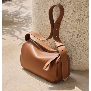 Brown leather cylinder shoulder bag with wide strap and gold hardware in natural outdoor light