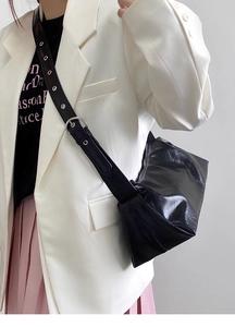 Detail of glossy black leather handbag showing wide strap with large silver buckle