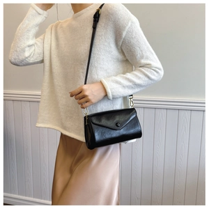 Detail of black envelope crossbody bag with gold hardware worn by a model in a minimal setting
