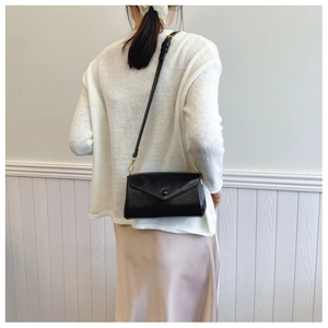 Detail of vintage black envelope crossbody bag with a triangular flap on a white dress