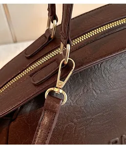 Détail de sac en cuir grainé marron foncé avec fermeture éclair dorée et mousquetons mobiles