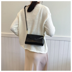 Classic black crossbody bag with flap and gold hardware on woman in white sweater