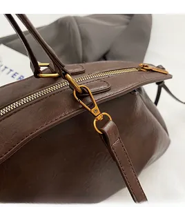 Gros plan du sac en cuir marron foncé montrant les fermetures éclair et crochets dorés