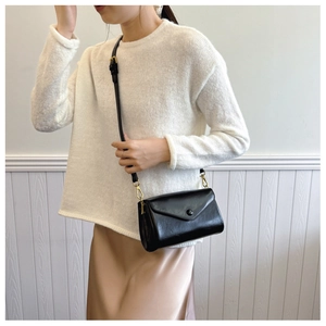 Detail of a black crossbody bag with flap and gold hardware on an elegant model