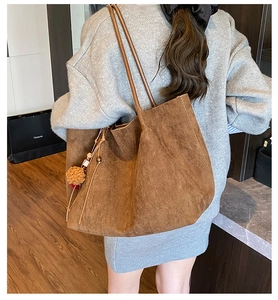 Detail of large brown suede tote bag with fringe charm on shoulder strap