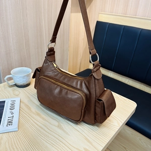 Retro deep brown shoulder bag with multiple zippers on a wooden table, minimalist style