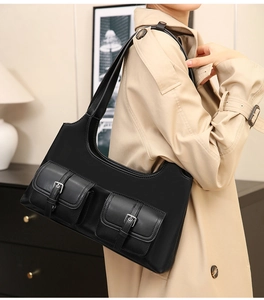 Detail of black matte leather shoulder bag featuring dual pockets with silver buckle accents
