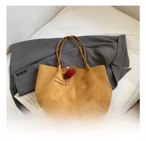 Detail of camel suede tote bag with brown leather base and red pompom tassel