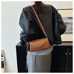 Brown vintage leather shoulder bag with flap closure and round buckle on a female model