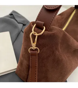 Detail of brown suede handbag featuring gold-tone lobster clasp and leather strap