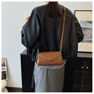 Close-up of brown leather crossbody bag with envelope flap and adjustable strap on a model