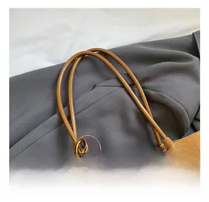 Detail of caramel suede tote bag with round leather handles and a dark red pompom charm