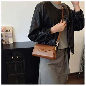 Brown leather envelope crossbody bag with adjustable strap worn by model in minimalist room
