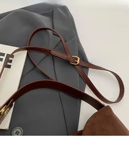 Detail of adjustable brown leather shoulder strap with gold buckle on a matte handbag