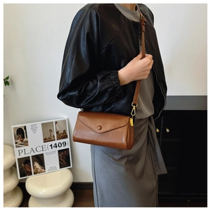 Detail of a brown leather envelope crossbody bag with gold hardware on a model