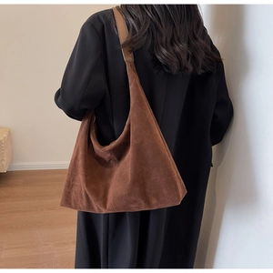 Détail macro du sac cabas en daim marron montrant la texture et la bandoulière sur modèle
