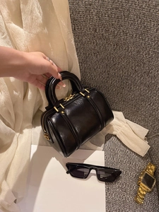 Detailed close-up of glossy black barrel bag with premium gold zipper and metal hardware