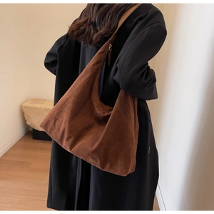 Vue de dos d'un modèle portant un grand sac hobo en daim marron mat avec large bandoulière