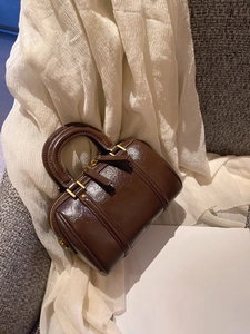 Close-up of a glossy dark brown mini Boston bag with gold hardware and shiny patent finish