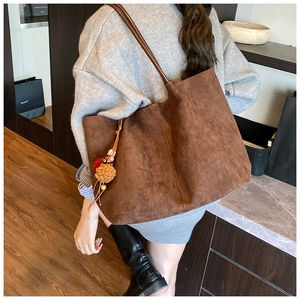 Close-up of a large brown suede tote bag with decorative colorful charms on the shoulder