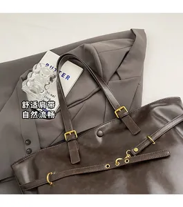 Detail of dark brown leather tote bag showing gold buckle and snap closure on a grey blazer