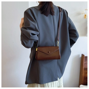 Detail view of a brown leather shoulder bag styled with a grey blazer and skirt