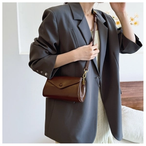 Detail of dark brown vintage leather crossbody bag with gold hardware on casual outfit