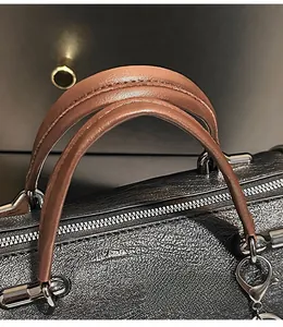 Dettaglio dei manici in pelle marrone e finiture in metallo argento di una borsa Boston