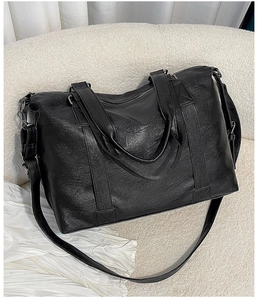 Detailed close-up of large black leather travel bag with adjustable strap and dual handles