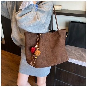 Detail of a large brown suede tote bag with a decorative plush charm for autumn style