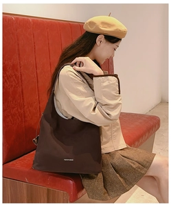 Borsa tote marrone in tela con scritte indossata da una modella su una panca vintage