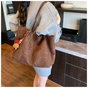 Detail of dark brown faux suede tote bag with plush pom-pom charm and slim shoulder straps