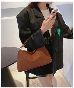 Detail of caramel brown suede handbag with adjustable leather handle on a black blazer